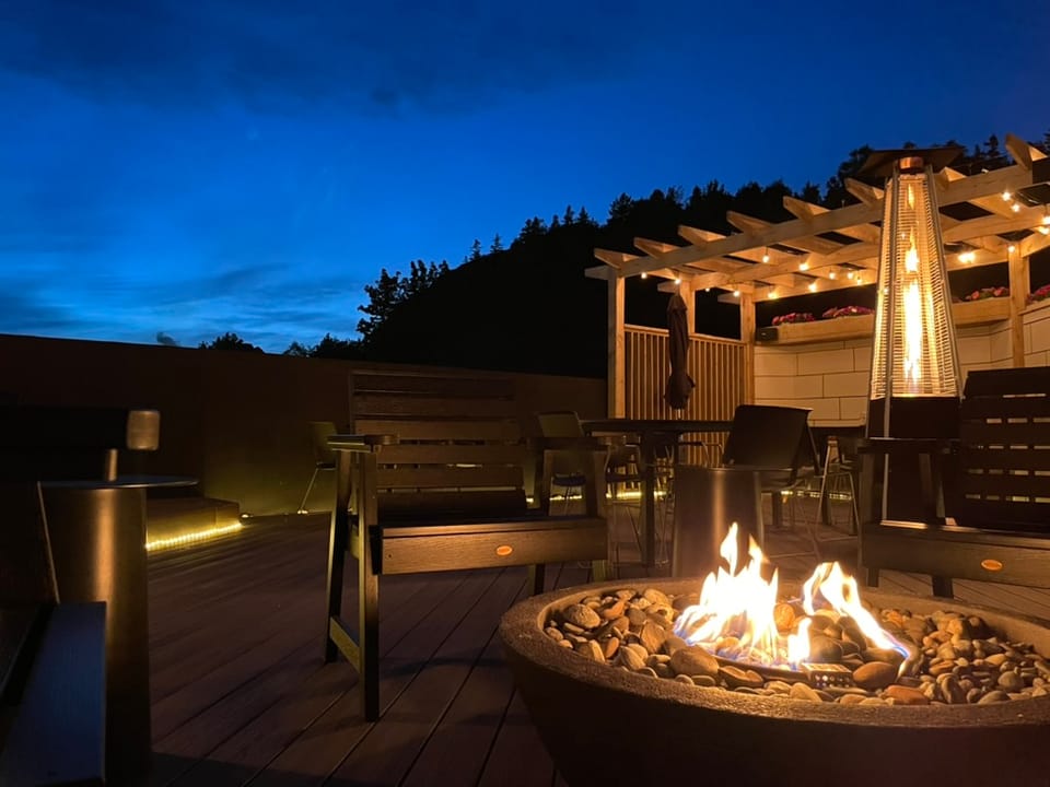 A twilight sky sits behind a patio that is lit by a central fireplace, a tall heater, and warm lighting.